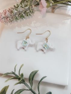 the earrings are white and have blue beads on them, along with some pink flowers