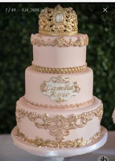 a three tiered pink cake with gold trimmings and a crown on top