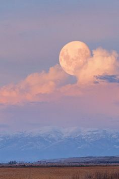 the full moon is setting in the sky above mountains