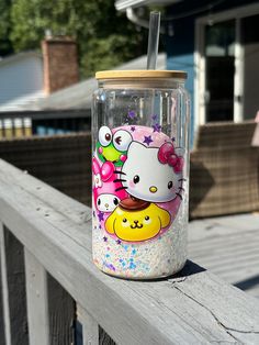 a hello kitty drink cup sitting on top of a wooden fence