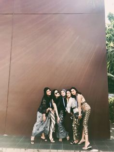 three women standing next to each other in front of a brown wall with palm trees