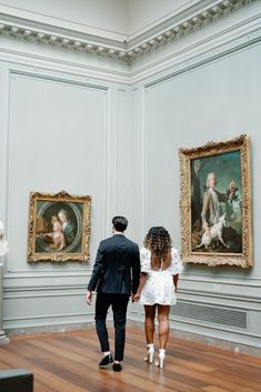 a man and woman looking at paintings in a museum