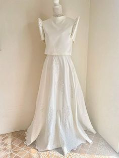 a white wedding dress hanging on a wall in a room with tile flooring and walls