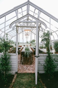 an outdoor dining area with tables and chairs under a white tented structure surrounded by greenery