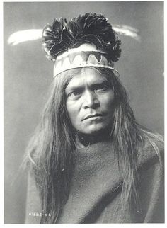 an old black and white photo of a man with long hair wearing a headdress