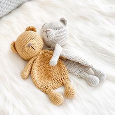 two crocheted teddy bears laying on top of a white fur covered bed next to each other