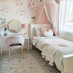 a bedroom decorated in pink and white with flowers on the wall behind the bed, desk, mirror and chair