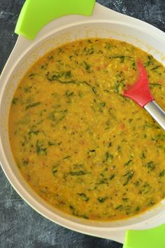 a white bowl filled with soup on top of a green and yellow table cloth next to a red spatula