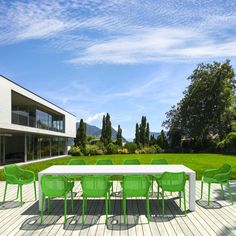 a white table with green chairs on a wooden deck in front of a large building