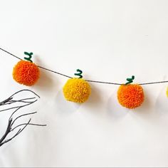 an orange and yellow pom - pom garland hanging from a wire with two small pumpkins attached to it