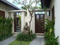 a buddha statue sitting in the middle of a garden next to a building with wooden doors