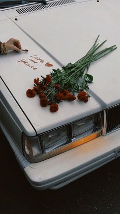 someone is writing on the hood of a car with flowers in front of it,