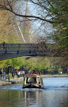 a boat traveling down a river under a bridge with people walking on the other side