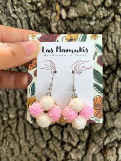 the pink and white pom - pom earrings are on display in front of a tree