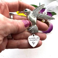 a person holding a silver bird with a heart shaped keychain on it's finger