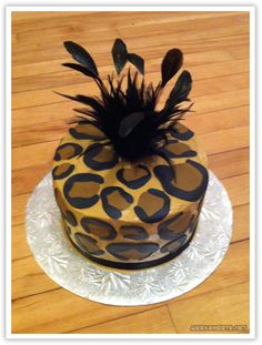 a cake decorated with black feathers and leopard print on a white plate sitting on a wooden floor