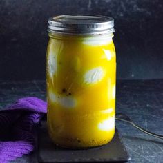 a jar filled with yellow liquid sitting on top of a table next to a purple towel