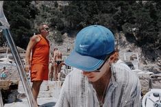 a man wearing a blue hat and sunglasses standing next to a woman in an orange dress