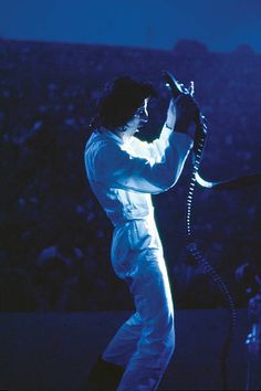 a man in white performing on stage with his hands up to the sky and holding a microphone