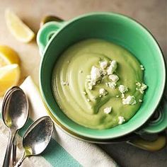 a green bowl filled with food next to sliced lemons and spoons on a table