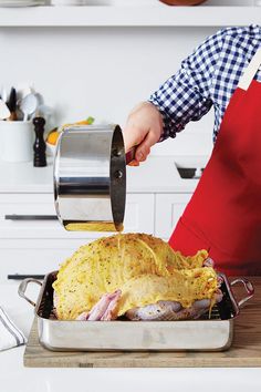 a person pouring gravy on top of a turkey in a roasting pan