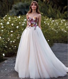 a woman in a white dress with flowers on the bouncy skirt is standing outside