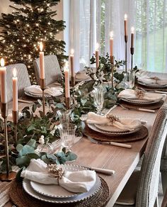 a dining room table set for christmas with candles and greenery on the table top