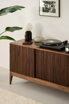 a record player sitting on top of a wooden cabinet next to a potted plant