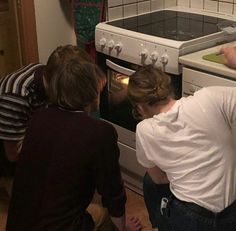 three people are looking into an oven in the kitchen