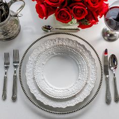 the table is set with silverware and red roses