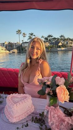 a woman sitting at a table with a cake and flowers in front of her on the water