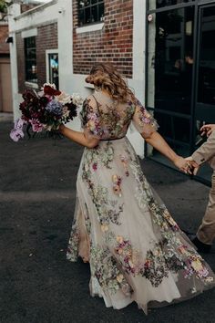 a man and woman holding hands walking down the street with flowers on their dress sleeves