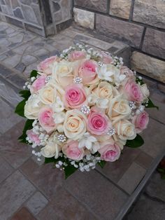 a bridal bouquet with pink and white flowers on a stone floor in front of a brick wall