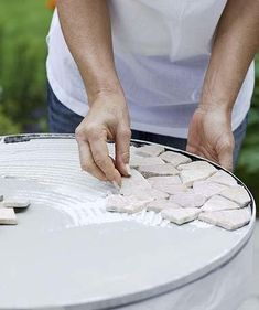 a man is placing small pieces of white tile on top of a round metal table