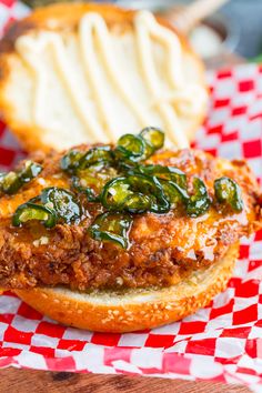 a sandwich with meat and vegetables on it sitting on a checkered table cloth next to a roll