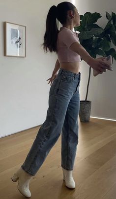 a woman standing in front of a potted plant on top of a hard wood floor