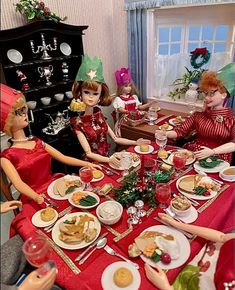 several dolls sit around a table with food and wine glasses on it for christmas dinner