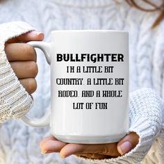 a woman holding a white coffee mug with the words bullfighter in a little bit country, a little bit rodeo, and a whole lot of fun