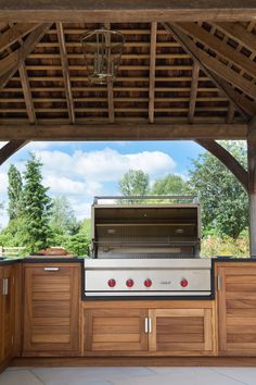 an outdoor kitchen with wood cabinets and a grill on the counter top, under a pergolated roof