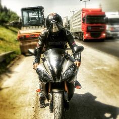 a man riding on the back of a motorcycle down a road next to a red truck