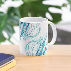 a white and blue coffee mug sitting on top of a wooden table next to a book