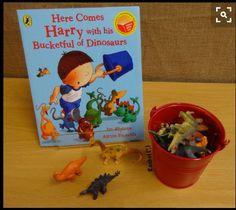 there is a book and toy dinosaurs next to it on the table with a red bucket