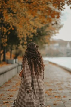 a woman is walking down the street with an umbrella in her hand and some leaves on the ground