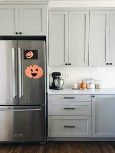 a stainless steel refrigerator in a kitchen with white cabinets and wood flooring, decorated for halloween