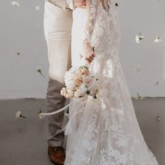 the bride and groom are holding each other's hands as they stand in front of white flowers