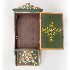 an old wooden box with floral designs painted on the side and inside, sitting against a white wall