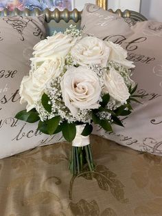 a bouquet of white roses sitting on top of a bed next to pillows and pillow cases