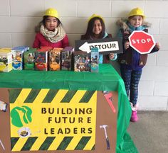 three children standing behind a table with books on it and holding signs that read building future leaders