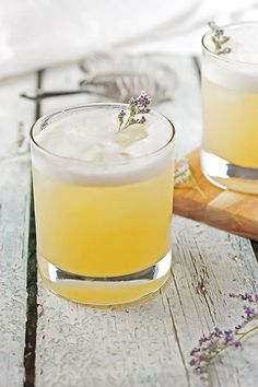 two glasses filled with yellow liquid and lavender sprigs on a wooden table next to a cutting board