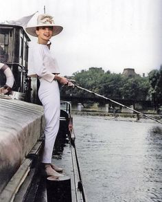 a woman standing on the side of a boat while holding onto a fishing rod and wearing a hat